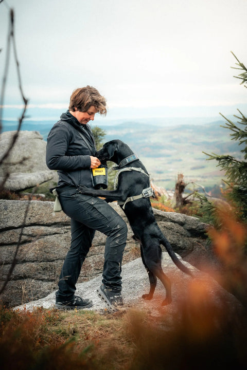 Psí trenérka na výšlapu se svým psem, dávající Dogule psí pamlsek